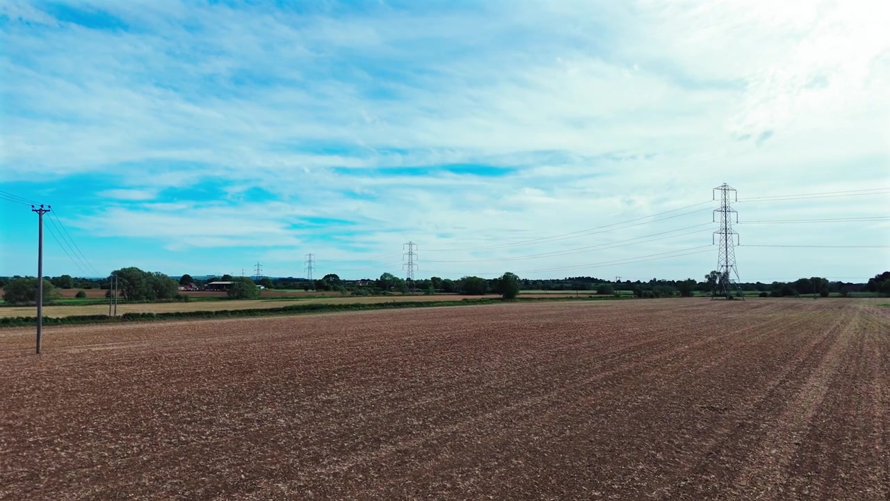 Eine weite Aufnahme, die von Strommasten in der britischen Landschaft an einem sonnigen Tag nach links schwenkt und aufsteigt