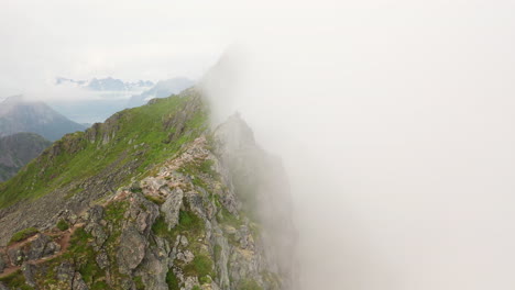 cinematic revealing drone shot mountain ridge through the clouds, fløya and djevelporten above svolvær in lofoten, norway, aerial footage