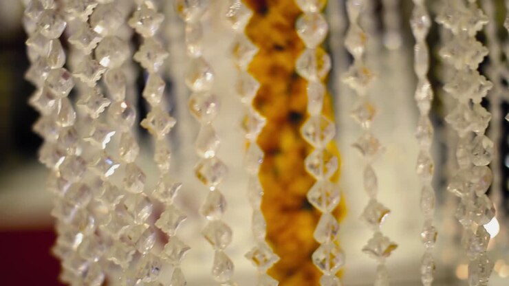 Catena di perline acriliche trasparenti per addobbi nuziali attorno a fiori color oro, primo piano