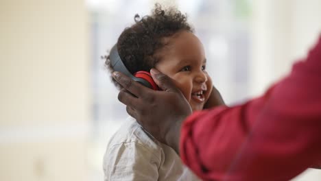 retrato de un alegre niño afroamericano sonriente de cabello rizado con ojos marrones escuchando música en auriculares con manos masculinas quitando los auriculares.