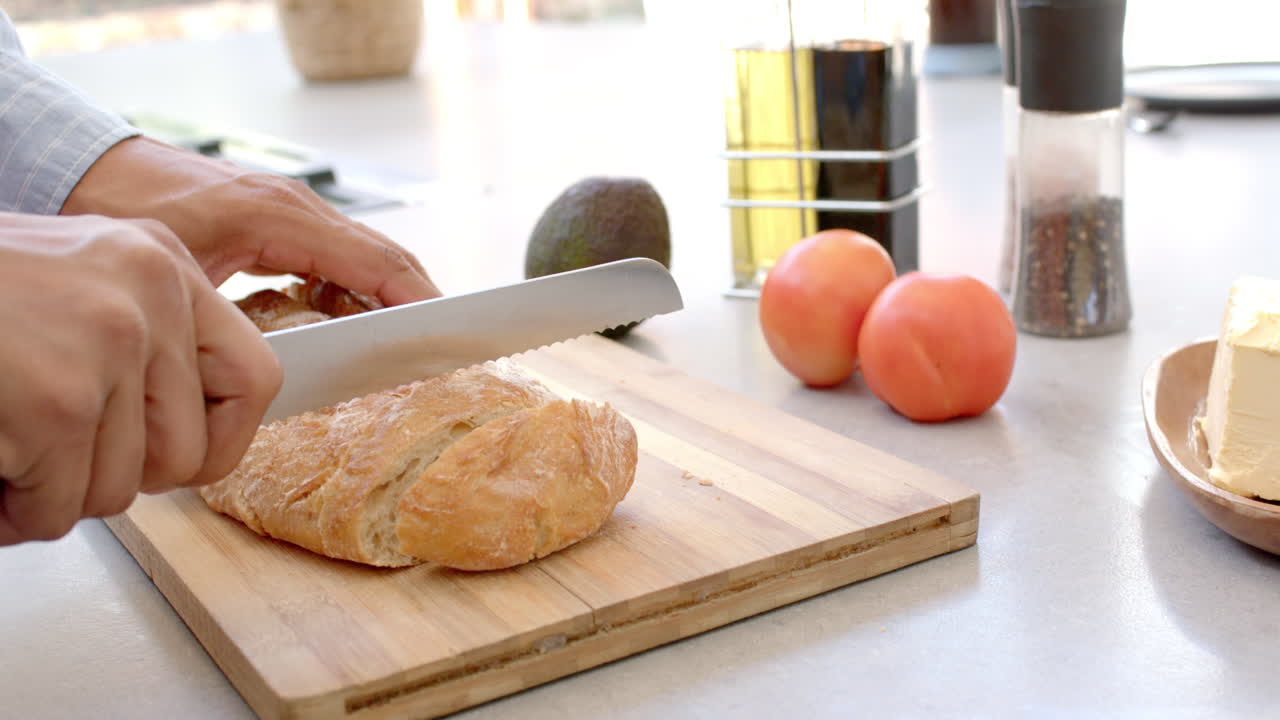Cutting bread on wooden board, person preparing meal with avocado and tomatoes