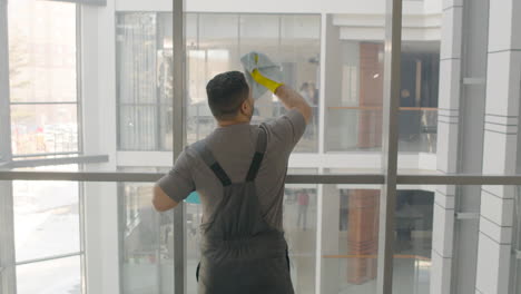 rear view of arabic cleaning man cleaning the window panes with a rag and glass cleaner inside an office