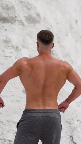 back view of athlete with muscular body outdoors. healthy body of a bodybuilder on white mountain background. vertical video