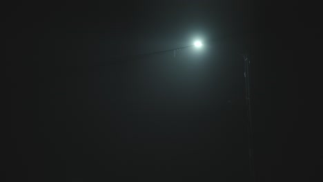 Streetlamp-light-greenish-spot-outside-during-pitch-black-night-with-spooky-fog-atmosphere