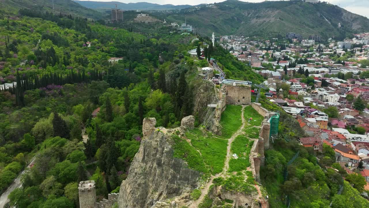 A scenic aerial view of the Narikala Fortress and green Tbilisi hills during springtime, showcasing the city’s natural beauty and history