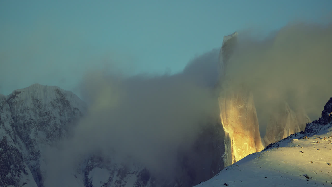 Časosběrné video Cerro Torre vynořujícího se z mraků, s teplým slunečním světlem kontrastujícím s chladnými alpskými podmínkami v jižní Patagonii