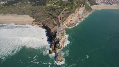 Klippe-Am-Strand-Von-Nazare-Mit-Einem-Leuchtturm,-Der-Hoch-Auf-Dem-Felsigen-Hügel-Steht