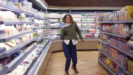 Imágenes-Completas-De-Una-Mujer-Joven-Con-Jeans-Y-Suéter-Bailando-Parada-En-El-Pasillo-De-Una-Tienda-De-Comestibles-Con-Una-Gran-Variedad.-Mujer-Emocionada-Divirtiéndose,-Bailando-En-El-Supermercado.-Camara-Lenta