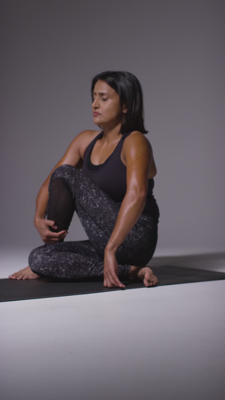 피트니스 옷을 입은 성숙한 여성이 바닥에 앉아 필라테스 스트레칭 운동을 하는 수직 비디오 스튜디오