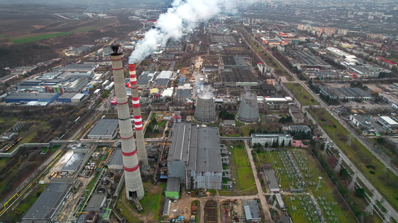 Aerial drone view of thermal power plant in Chisinau at cloudy weather, Moldova. View of pipes with felling steam, buildings and yellowed trees around
