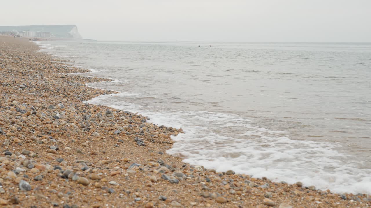 Toma a cámara lenta de la costa rocosa de guijarros de Seaford con rocas en primer plano y acantilados de creta blancos al fondo.