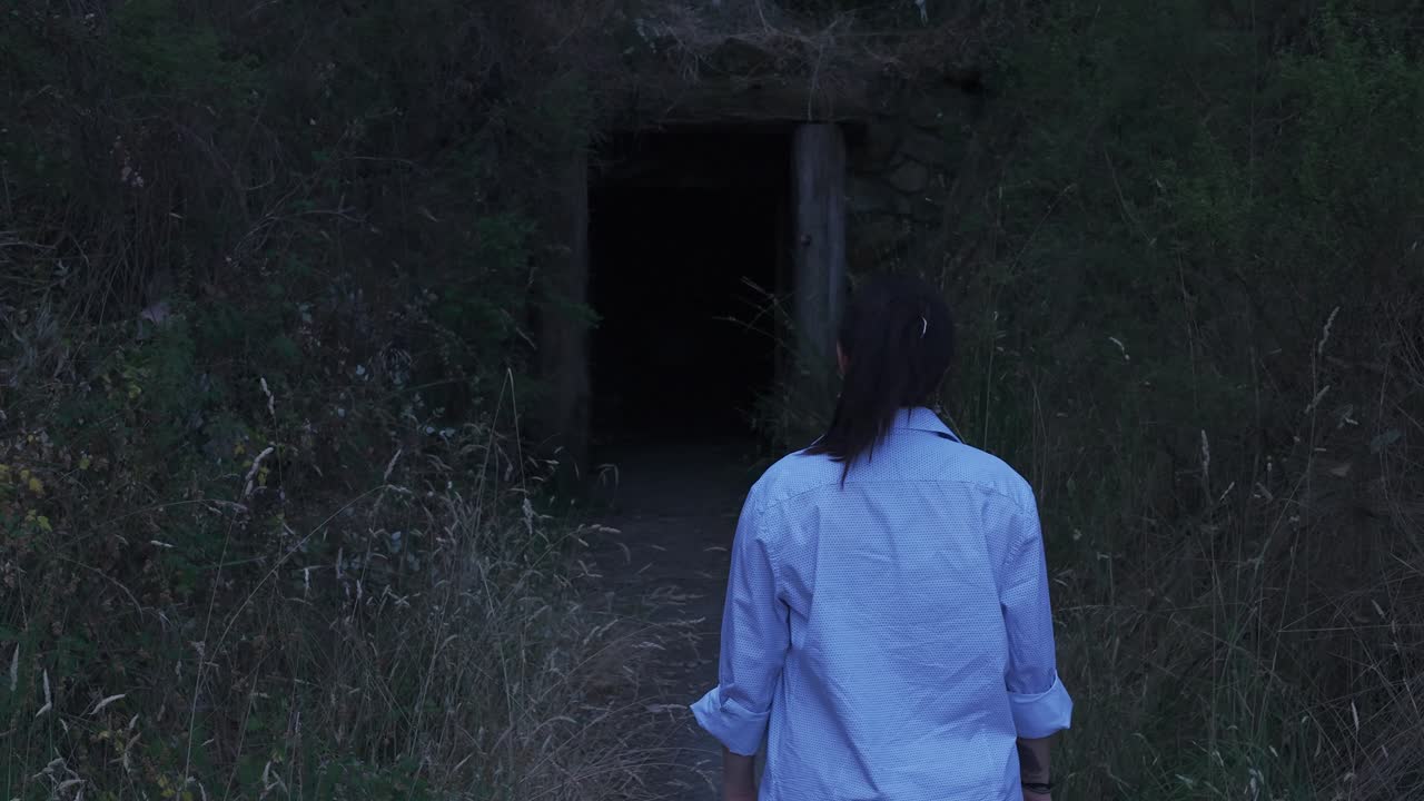 A girl stands before a dimly lit mining tunnel entrance in Warrandyte Park, Melbourne. The twilight sun casts a mysterious glow over the scene, capturing a moment of intrigue and exploration