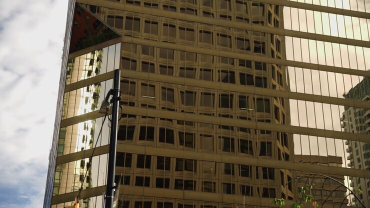 Tom fechado em câmera lenta revelando um arranha-céu de hotel dourado cheio de janelas de vidro espelhado com tom dourado. Contrastado com o céu azul e nuvens ao fundo. Muitas reflexões nas janelas
