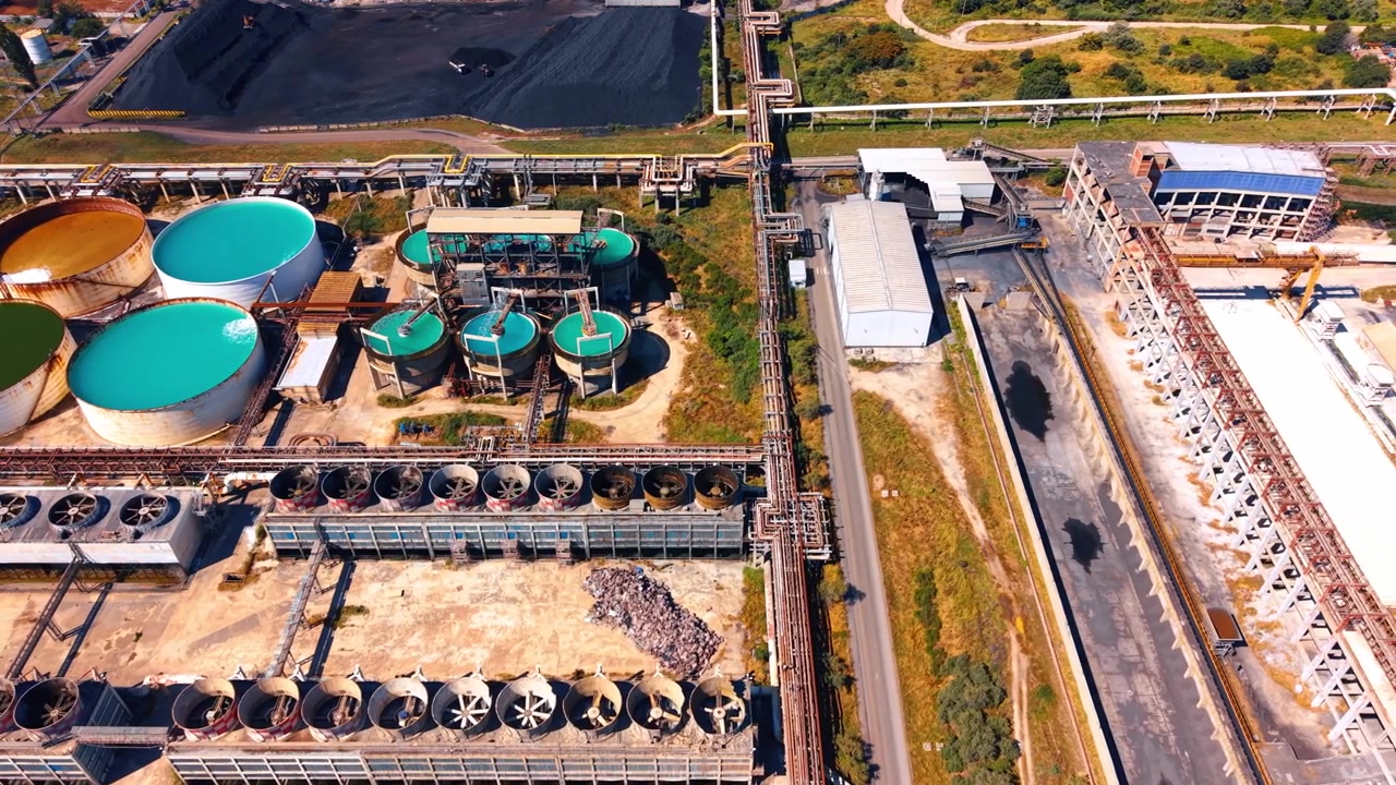Industrial water treatment tanks and cooling fans. Round liquid storage basins sit near row of cooling fans and metal pipelines at factory.