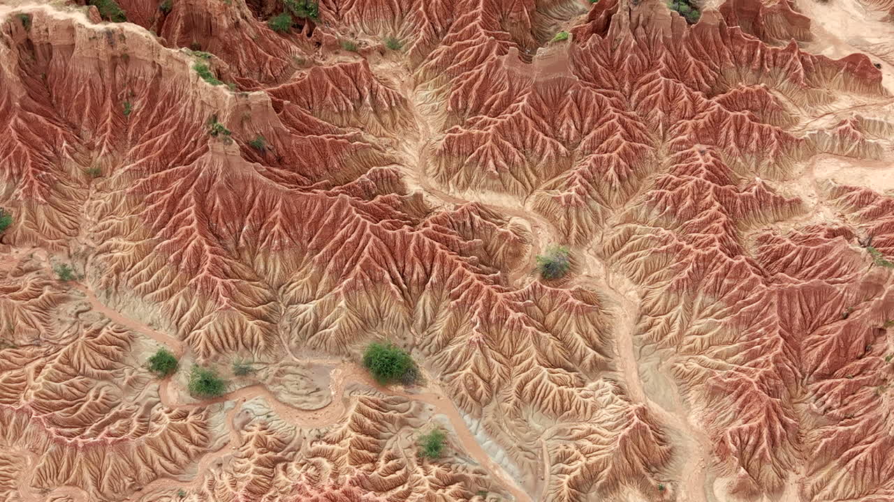 Drone video capturing the vibrant red and orange erosion patterns of Tatacoa Desert, showcasing a dramatic, sunlit landscape with intricate details in a sweeping natural formation.