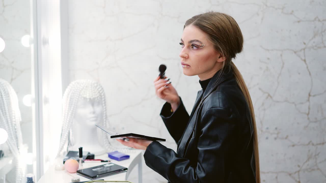 Woman applying eye makeup with glitter in front of a mirror
