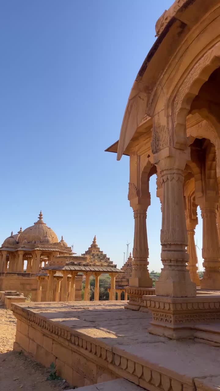 A forward-moving shot of Bada Bagh in Jaisalmer, Rajasthan, showcases its stunning cenotaphs and architecture glowing under a clear, sunny desert sky, reflecting the grandeur of royal heritage