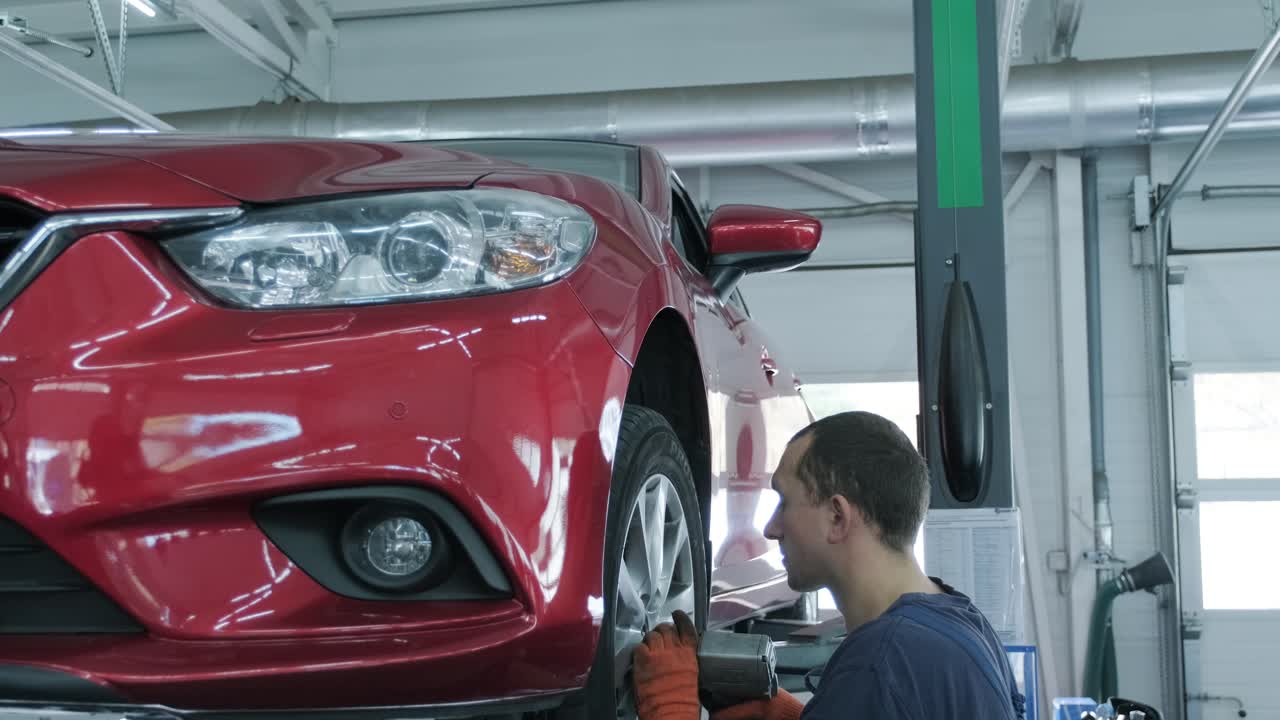 mecánico de automóviles atornillado o desenroscado de la rueda del automóvil levantado en la estación de servicio de reparación