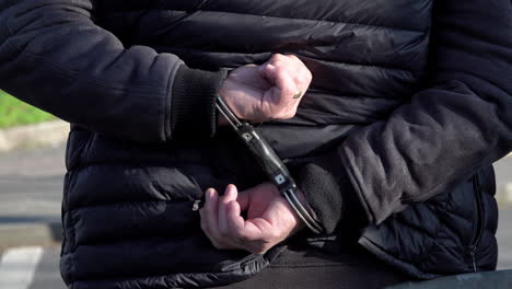 a person stands detained with his hands restrained with speed cuffs behind his back