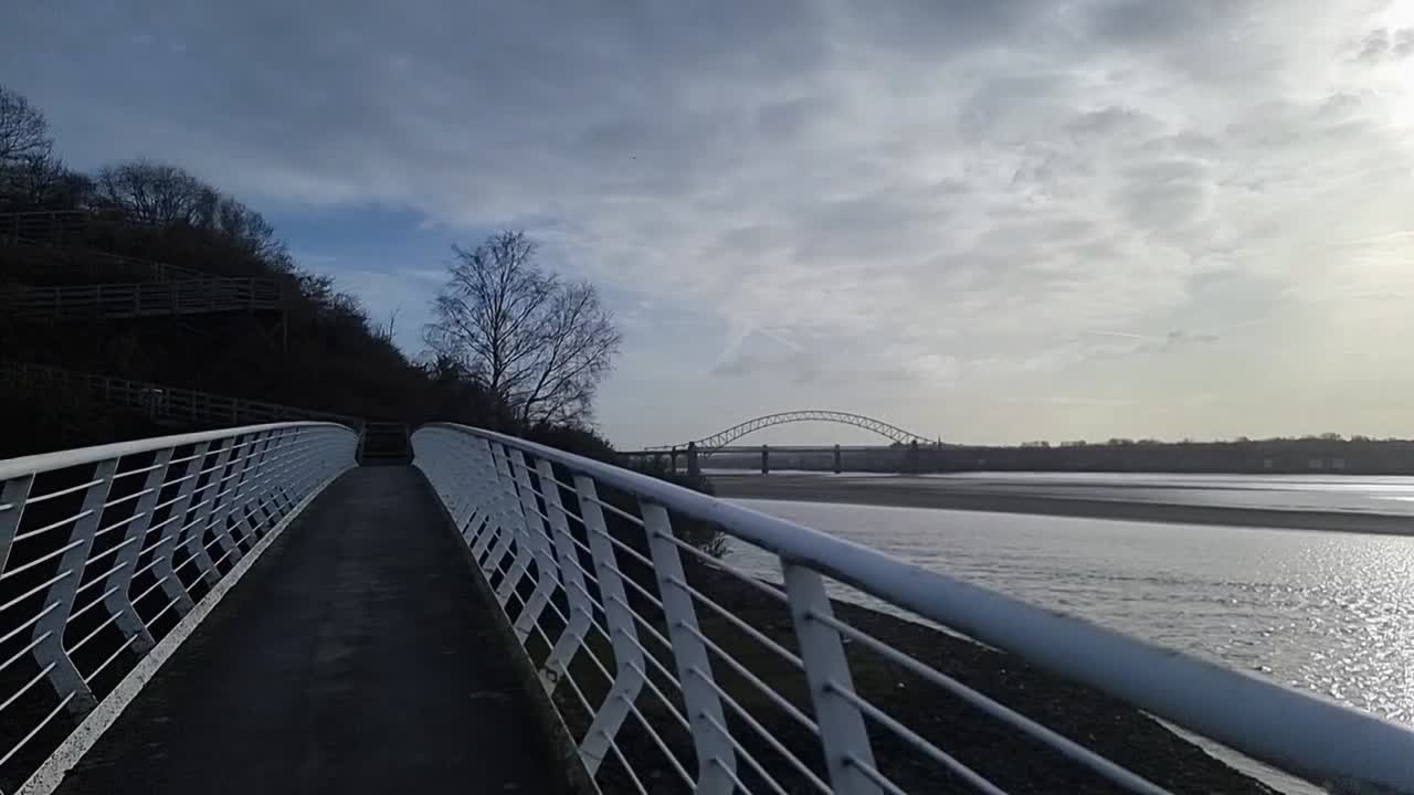 Panning across River Mersey shimmering estuary at sunrise under the Runcorn arched bridge crossing