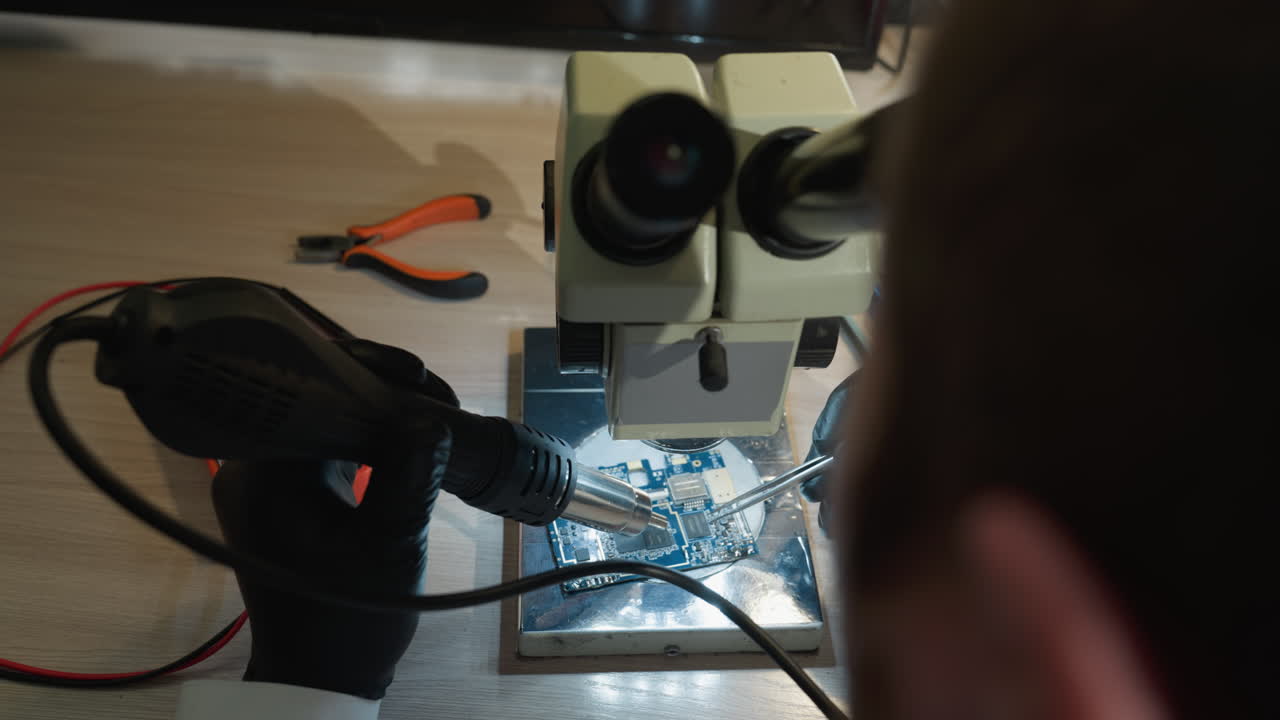 una vista de cerca de un técnico trabajando en una placa de circuito, la mesa está esparcida con varias herramientas de reparación electrónica, incluido un multimetro, un soldador y destornilladores de precisión