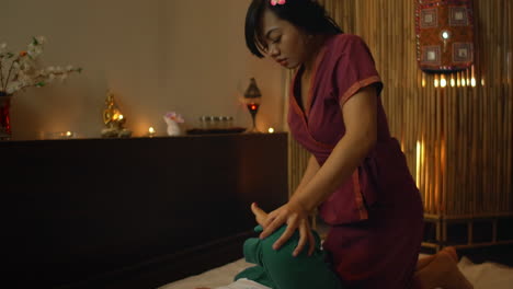 portrait of relaxed asian beautiful woman massaging neck and shoulder by professional massager in spa salon. body care treatment by thai massage. cute girl with traditional dress.