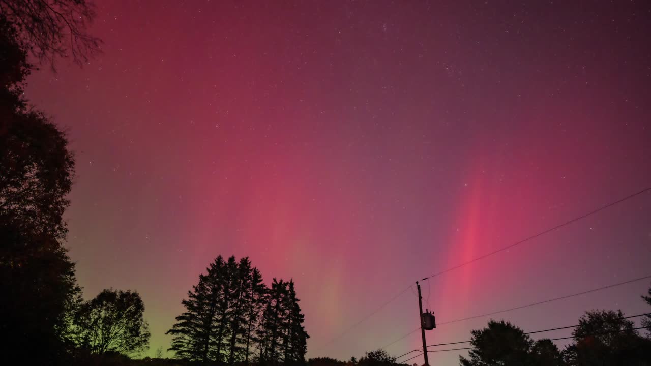 Aurora Borealis (northern lights) appearing over a backyard in New Hampshire during a major solar storm in August 2024. It has pinks, blues and greens dancing in the sky in this timelapse.