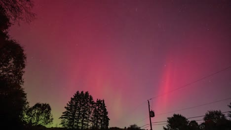 aurora borealis (northern lights) appearing over a backyard in new hampshire during a major solar storm in august 2024. it has pinks, blues and greens dancing in the sky in this timelapse.