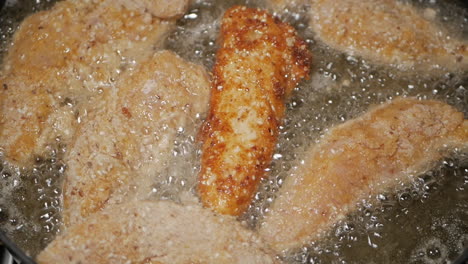 crumbed breast chicken tenderloins being placed in peanut oil in a pan