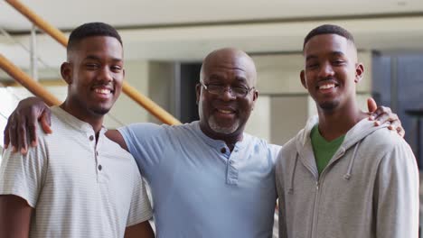 portrait of african american senior father and twin teenage sons embracing and smiling