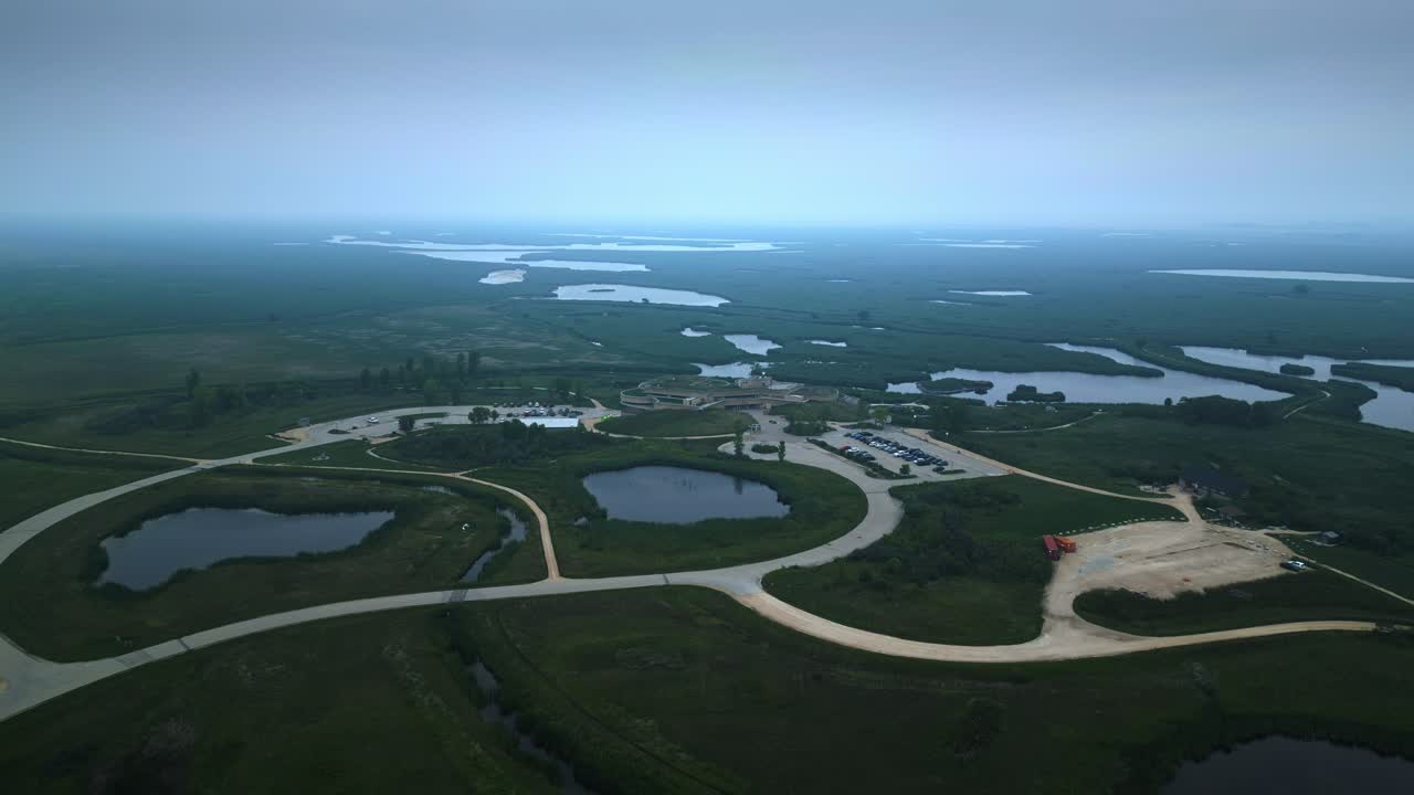 Drone moves toward eco centre with marshland context, establishing view