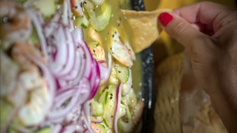 primer plano de una mano femenina atrapando un camarón usando un barco de tortilla en un plato tradicional mexicano llamado aguachile