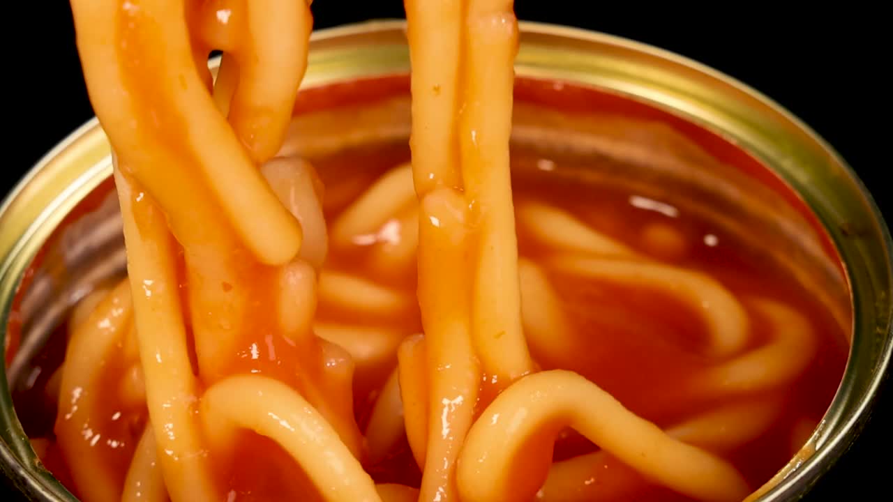 開いた缶詰から、木製の箸がソースのかかったスパゲッティ麺を掴んでいるマクロ撮影。