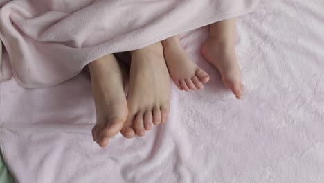 Two-pairs-of-legs-of-the-family-in-bed-under-the-coverlet---mother-and-baby