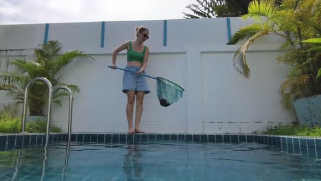 woman cleaning pool with pool skimmer