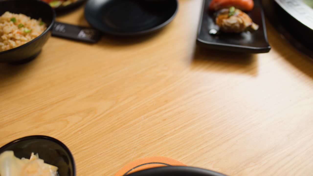 Hand places salmon sushi hand roll in wooden holder on restaurant table, natural lighting, close-up