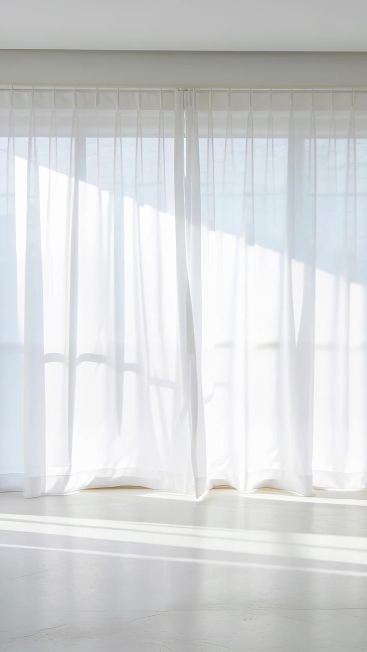 Video verticale: Tende velate che ondeggiano e si muovono su alte finestre in studio, la brezza sposta una fascia di luce.