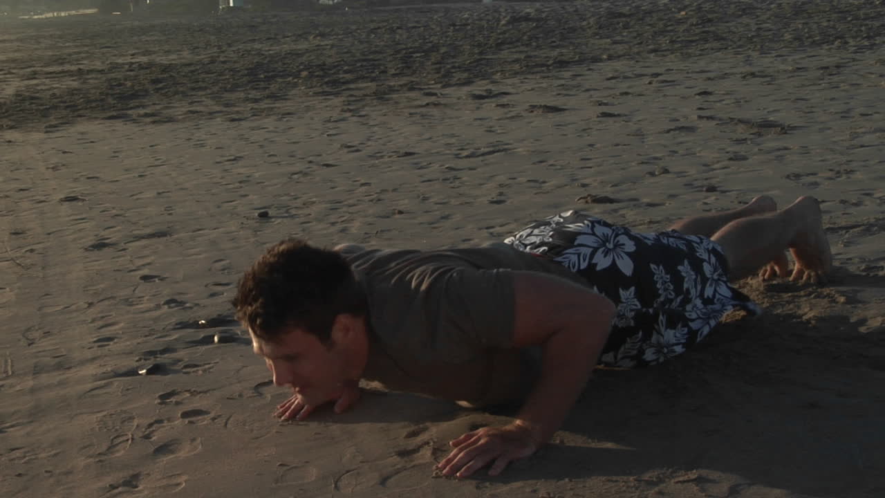 un hombre hace flexiones en una playa de arena