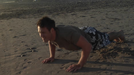 un hombre hace flexiones en una playa de arena