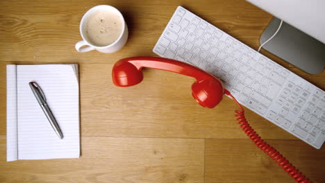 Red-phone-receiver-falling-onto-office-desk