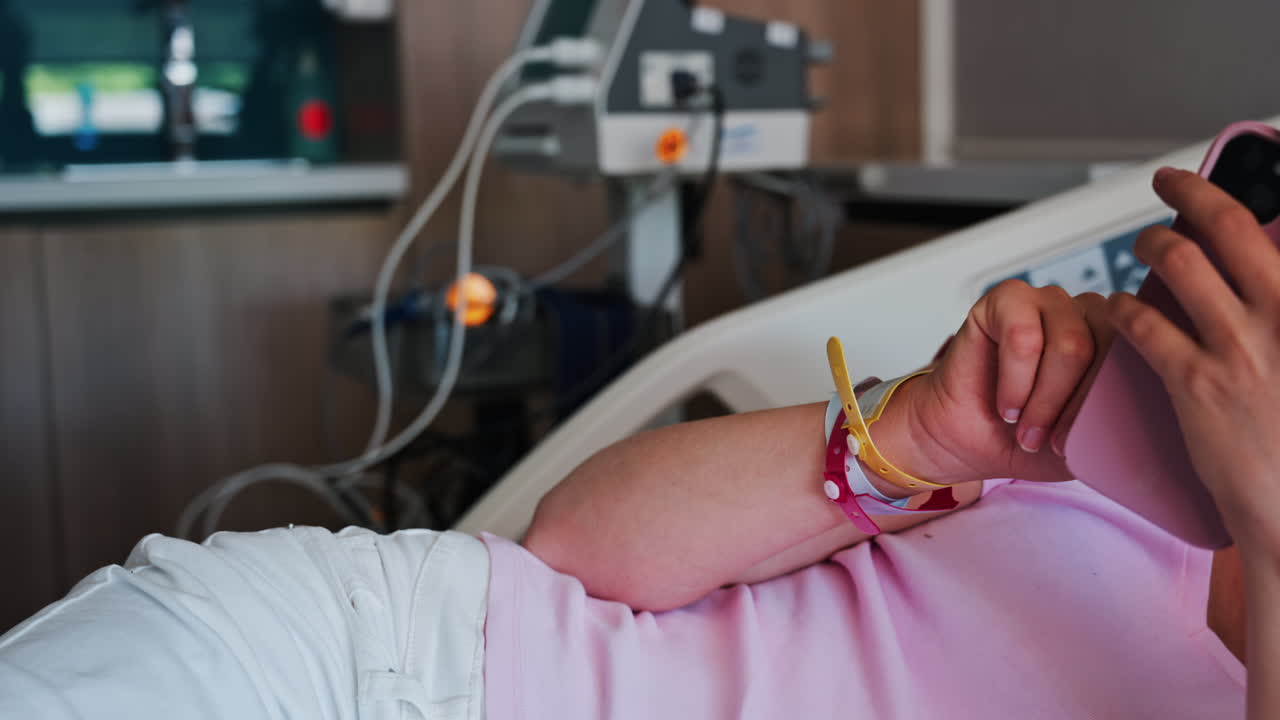Pregnant woman scrolling on her phone while lying in a hospital bed at the doctor's office