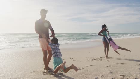 happy hispanic parents playing with children on beach in sun