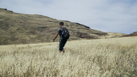 Hombre-Caminando-Por-El-Campo-De-Hierba-Dorada-Con-Mochila,-Cámara-Lenta