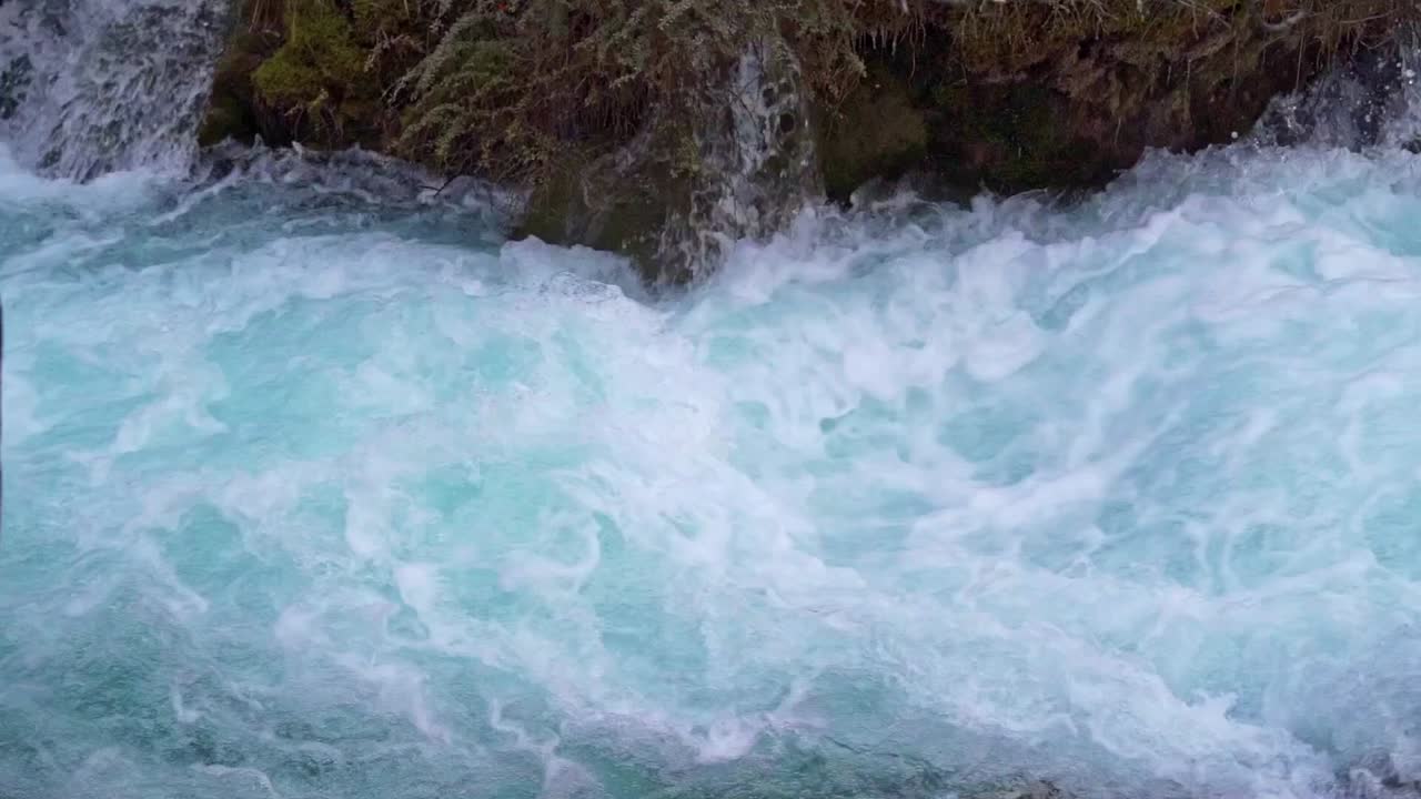 Jiuzhaigou Milli Parkı'nda köpüren turkuaz su ve hırçın akıntıların detaylı, yüksek açılı yakın çekimi, yosunlu kayaların arasından hızla akan bir dağ nehrinin güçlü enerjisi ve sıçrayan köpükleri