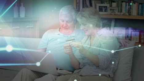 glowing network of connections against senior caucasian couple holding credit card using laptop