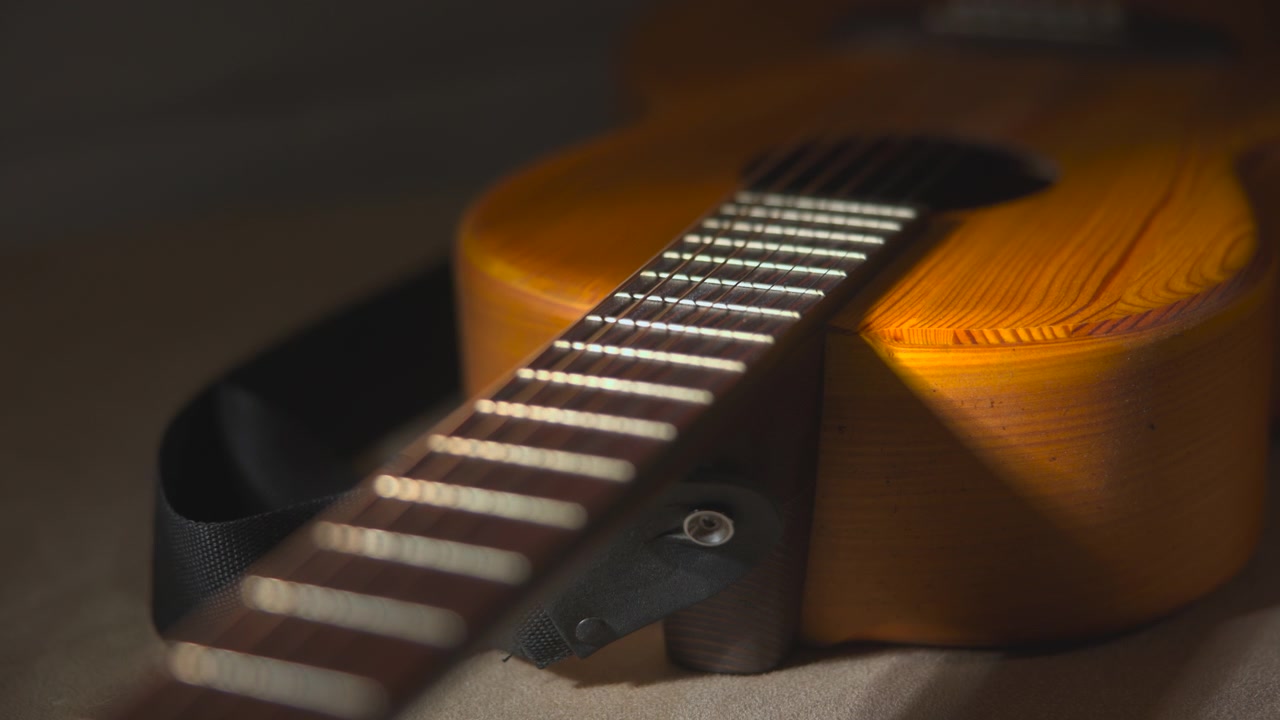 Keskin odakta bir gitar klavyesinin çapraz yakın çekimi, arkasında enstrümanın gövdesi yumuşakça bulanıklaşmış, sıcak kehribar rengi bir arka plana karşı konumlandırılmış, bu da bir etki yaratıyor.