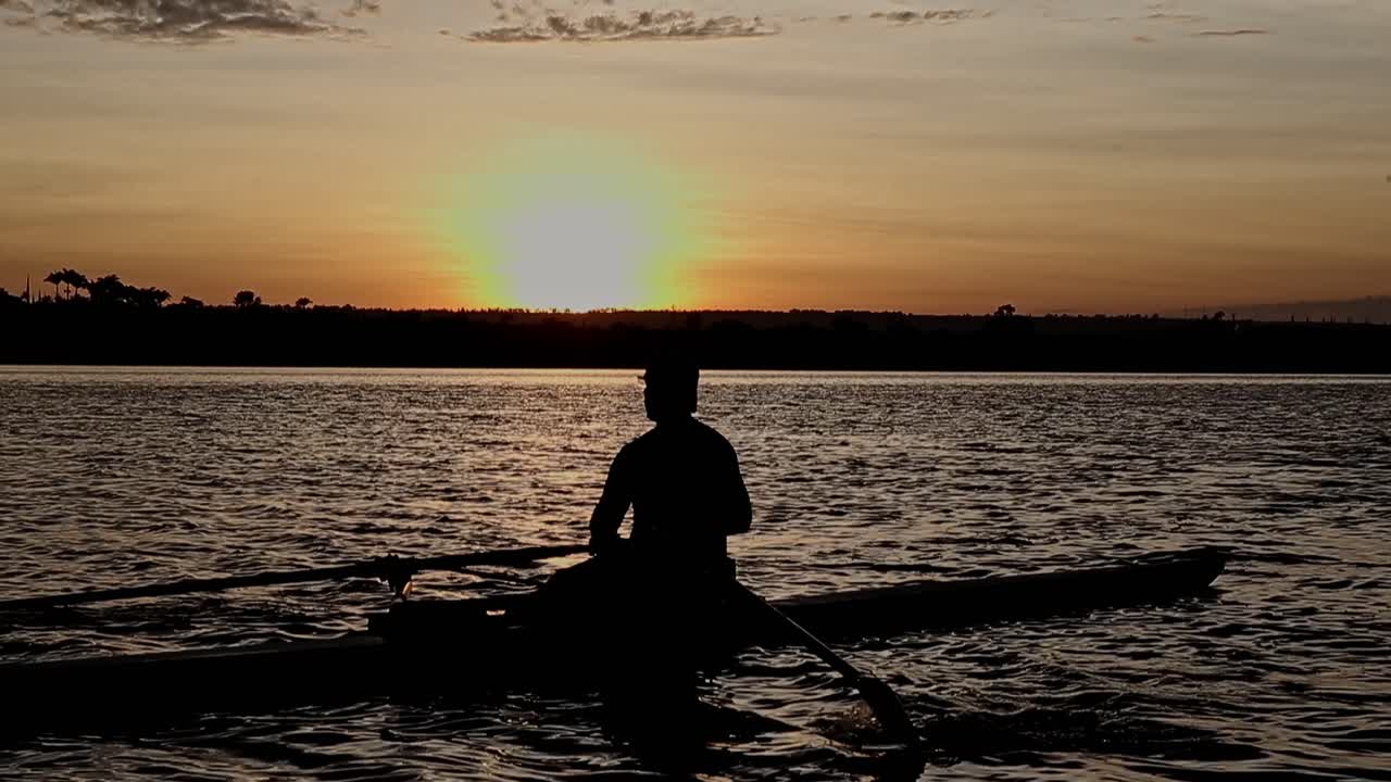 silueta de primer plano de un atleta masculino en un bote de remo en un colorido entrenamiento en el lago al atardecer