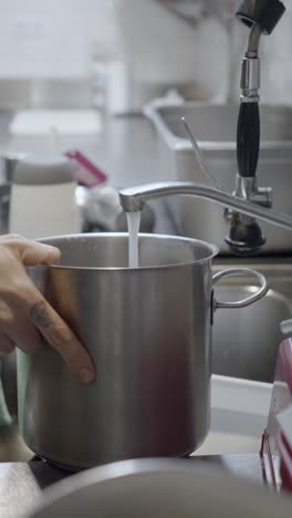 hands filling a pot with water in a commercial kitchen