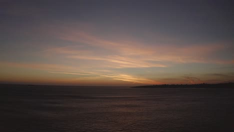 Aerial-view-over-many-surfers-in-Estoril,-sunset-in-Portugal---pull-back,-drone-shot