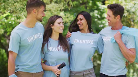 retrato de un grupo diverso de amigos sonrientes con camisetas azules voluntarias recolectando basura en el parque